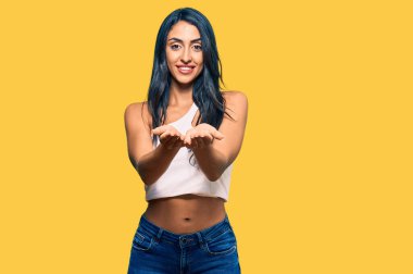 Güzel İspanyol kadın, sıradan kıyafetler giyip avuçlarını birbirine değdirip gülümseyerek jest yapıyor. Bekleme ve koruma 