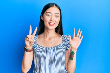 Genç Çinli kadın, günlük çizgili tişört giyer ve yedinci parmaklarını göstererek gülümserken kendinden emin ve mutlu.. 