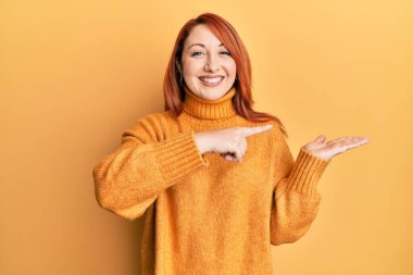 Güzel kızıl saçlı kadın, mutlu ve havalı bir gülümsemeyle avucunun içindeki boşluğu işaret ederek gülümsüyor. diş gösterme. 