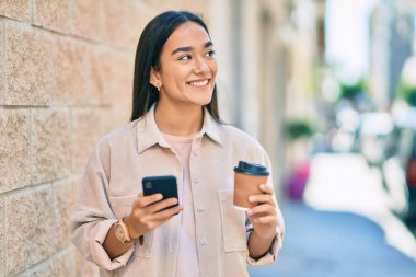 Genç Latin kız akıllı telefon kullanıyor ve şehirde kahve içiyor..
