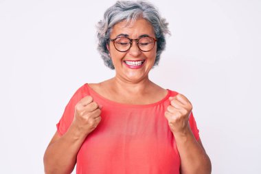 Son sınıf Latin kökenli gri saçlı, sıradan kıyafetler ve gözlük takan başarılı olmak için heyecanlanan kolları havada ve gözleri kapalı zaferi kutlayan bir kadın. Kazanan konsept. 