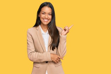 Güzel İspanyol kadın iş ceketi giyiyor, yüzünde kocaman bir gülümseme var, eli ve parmağı kameraya bakıyor.. 