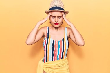 Bikini giyen genç, sarışın bir kadın ve kafasında el olan bir şapkası var. Stres yüzünden baş ağrısı çekiyor. migren ağrısı. 