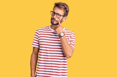 Sakallı, sıradan giyinmiş, gözlüklü yakışıklı bir adam. Gözünü dikip, jestini izliyor. Şüpheli bir ifade. 