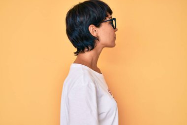 Güzel esmer kadın iğneleyici yorumlar giyip tişört yüklüyor. Tişörte bakıyor, rahat profil pozu veriyor. Kendine güvenen bir gülümsemesi var.. 