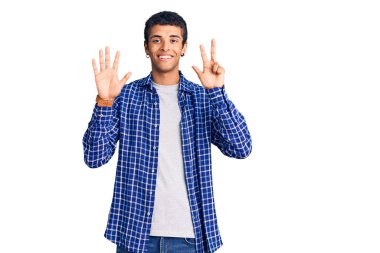 Genç Afrikalı Amerikalı günlük kıyafetler giymiş sekiz numaralı parmaklarıyla işaret ederken kendinden emin ve mutlu gülümsüyor.. 