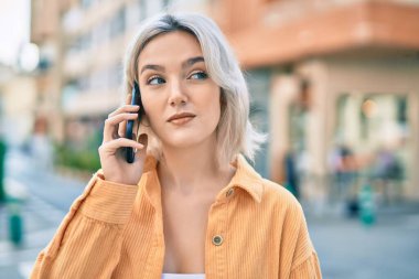 Rahatlamış yüzlü genç sarışın kız şehirde akıllı telefondan konuşuyor..