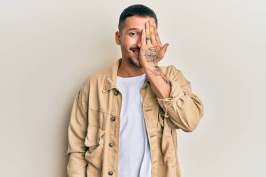 Dövmeli yakışıklı bir adam, günlük kahverengi kot ceket giyiyor, bir gözünü eliyle kapatıyor, yüzünde kendine güvenen bir gülümseme ve şaşırtıcı bir duygu var.. 