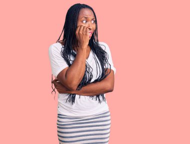 Rahat kıyafetler giyen genç Afro-Amerikalı kadın gergin ve gergin görünüyor. Ağzı tırnak yiyen ellerle. anksiyete. 