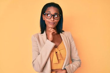 Genç Afro-Amerikalı kadın iş kıyafetleri giymiş, çenesi çenesine dayanmış soru soruyor, düşünceli bir ifade. Düşünceli bir yüzle gülümsüyor. şüphe kavramı. 