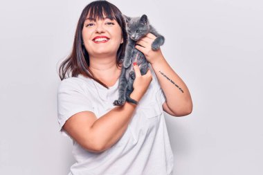 Genç, güzel, iri yarı, mutlu ve kendinden emin bir kadın. Yüzünde tebessümle durmuş, sevimli kediyi soyutlanmış beyaz arka planda tutuyor.