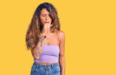 Dövmeli genç İspanyol kadın, günlük giysiler giyiyor kendini iyi hissetmiyor ve soğuk algınlığı veya bronşitin belirtisi olarak öksürüyor. sağlık hizmeti kavramı. 