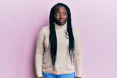 Saçları örgülü, sıradan bir kazak giyen genç siyahi kadın gülümseyerek yan tarafa bakıyor ve düşünüyor.. 