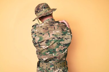 Kamuflaj üniforması giyen, mutlu ve pozitif bir şekilde kendini kucaklayan beyaz bir genç. Sevgi ve özgüven. 