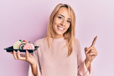 Güzel sarışın kadın elinde pasta tatlısı, gülümsüyor mutlu bir şekilde elini ve parmağını kenarda gezdiriyor. 