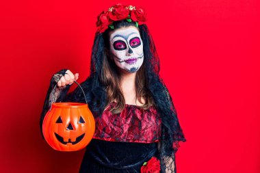 Ölü kostümü giymiş genç bir kadın elinde balkabağı tutarken pozitif ve mutlu görünüyor ve kendine güvenen bir gülümsemeyle dişlerini gösteriyor. 