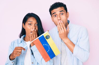 Venezuela bayrağını tutan genç ve güzel bir çift ağızlarını eliyle kapatıyorlar, şaşırmış ve hata yapmaktan korkuyorlar. şaşırmış ifade 