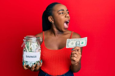 Genç Afro-Amerikalı bir kadın elinde kavanozla birikimlerini elinde tutuyor ve 1 dolarlık banknot kızgın ve öfkeli bir şekilde bağırıyor öfkeyle bağırıyor. öfke ve agresif konsept. 