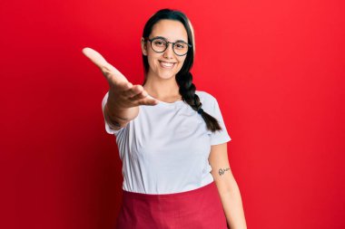 Genç İspanyol kadın profesyonel garson önlüğü giyip gülümseyerek selamlaşma ve dostça tokalaşma sunuyor. başarılı iş. 