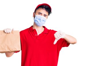 Teslimat üniforması giyen genç İspanyol bir adam ve elinde kızgın yüzlü bir çanta tutan tıbbi bir maske, olumsuz işaretler baş parmakları aşağıda, reddedilme konsepti var. 