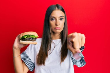 Genç İspanyol kadın kamerayı işaret ederek hamburger yiyor ve sen kendine güvenen ciddi bir hareket yapıyorsun. 