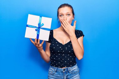 Sarışın genç bir kadın elinde hediyeyle ağzını eliyle kapatıyor. Şok olmuş ve hata yapmaktan korkuyor. şaşırmış ifade 