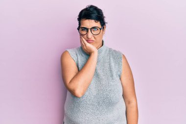 Artı, sıradan kıyafetler ve gözlük takan esmer kadın kollarını kavuşturarak depresyondan sıkılmış ve yorgun göründüğünü düşünüyor.. 