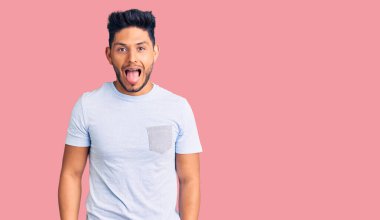 Yakışıklı Latin Amerikalı sıradan kıyafetler giyen genç adam komik bir ifadeyle dilini dışarı çıkartıyor. duygu kavramı. 