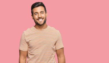 Yakışıklı, sıradan kıyafetler giyen, mutlu ve havalı bir gülümsemesi olan İspanyol bir adam. şanslı kişi. 