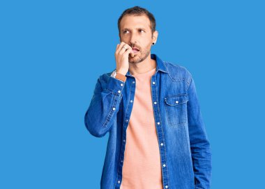 Günlük kıyafetler giyen genç yakışıklı adam gergin ve gergin görünüyor. Ağzı tırnak yiyen eller. anksiyete. 