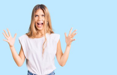 Sarışın, beyaz tişörtlü, güzel, beyaz bir kadın. Deli gibi bağırıyor, agresif bir ifadeyle bağırıyor ve kollarını kaldırıyor. hüsran kavramı. 