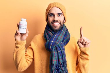 Sakallı, elinde hap şişesi olan genç yakışıklı bir adam bir fikirle gülümsüyor ya da bir soru işareti yapıyor. 