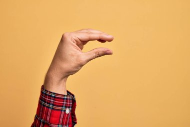 İzole edilmiş sarı arka plan üzerinde parmaklarını gösteren beyaz bir adamın eli. Görünmez bir şeyi alıp, parmaklarıyla uzayı gösteren bir nesneyi tutuyor.