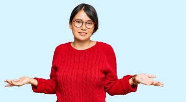 Kısa saçlı, sıradan bir süveter giyen, gözlüklü, kolları açık, kafası karışık, genç, İspanyol bir kadın.. 