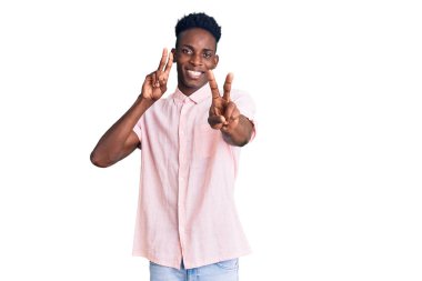 Gündelik giysiler giymiş, gülümseyen, parmaklarını zafer işareti yaparken gösteren genç bir Afro-Amerikan. İki numara.. 