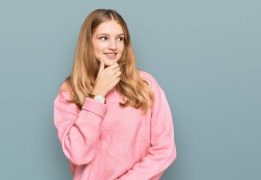 Güzel, genç, beyaz, sıradan bir kazak giyen, elleri çenesinde soru soran, düşünceli bir kız. Düşünceli bir yüzle gülümsüyor. şüphe kavramı. 