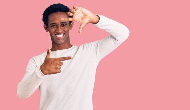 Sıradan bir kış süveteri giyen Afrikalı yakışıklı adam gülümseyerek elleri ve parmakları gülen yüzüyle çerçeve yapıyor. yaratıcılık ve fotoğrafçılık kavramı. 