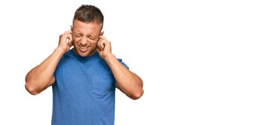 Yakışıklı, sıradan kıyafetler giyen, kulaklarını parmaklarıyla kapatan, gürültülü müzik sesi için rahatsız edici ifadeleri olan kaslı bir adam. sağır kavramı. 