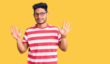 Yakışıklı Latin Amerikalı gündelik kıyafetler ve gözlük takan genç adam dokuz numarayı gösterip işaret ederken kendinden emin ve mutlu bir şekilde gülümsüyor.. 