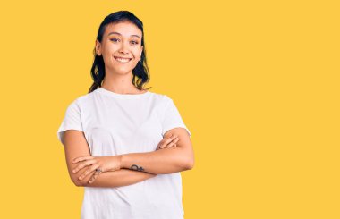 Sıradan kıyafetler giyen mutlu yüzlü, kollarını kavuşturup kameraya bakan genç bir kadın. pozitif kişi. 