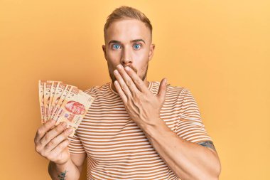 Meksika pesolarını elinde tutan genç beyaz adam ağızlarını eliyle kapatıyor, şaşırmış ve hata yapmaktan korkuyor. şaşırmış ifade 