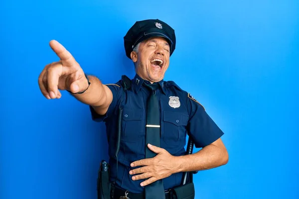 Handsome middle age mature man wearing police uniform laughing at you, pointing finger to the camera with hand over body, shame expression