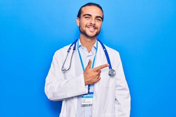 Jovem Homem Bonito Vestindo Casaco Médico Estetoscópio Sorrindo Alegre Apontando — Fotografia de Stock