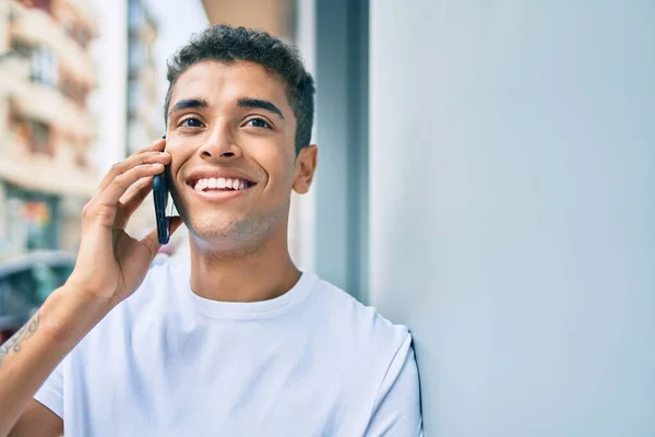 年轻的拉丁裔男子笑着高兴地在城市的智能手机上交谈 — 图库照片