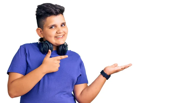 手で提示し 指で指している間 小さな男の子は 音楽を聞いて ヘッドフォンを身に着けている驚きとカメラに笑顔 — ストック写真