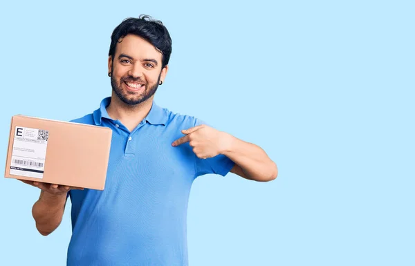 Mladý Hispánec Držící Doručovací Balíček Ukazující Prstem Jednoho Samolibého Šťastného — Stock fotografie