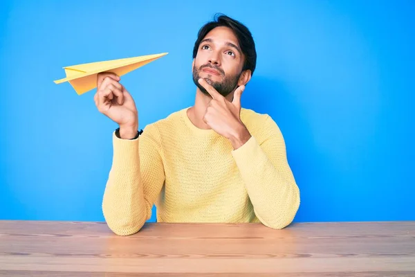 Hombre Hispano Guapo Sosteniendo Avión Papel Cara Seria Pensando Pregunta —  Fotos de Stock