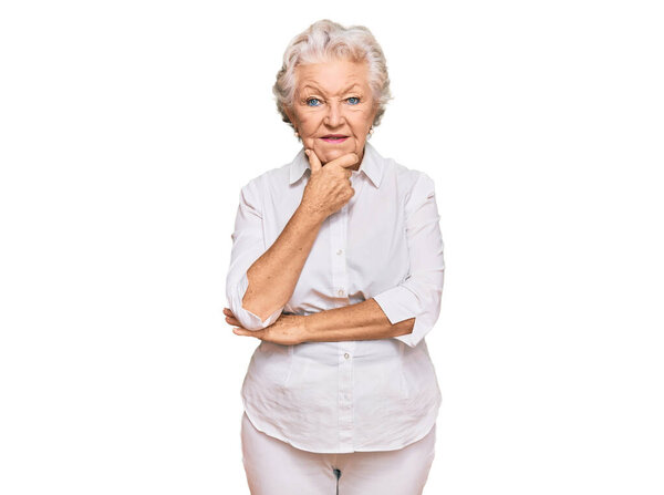 Старшая седовласая женщина в повседневной одежде, уверенно смотрящая на камеру, улыбаясь со скрещенными руками и поднятой на подбородок рукой. Позитивное мышление. 