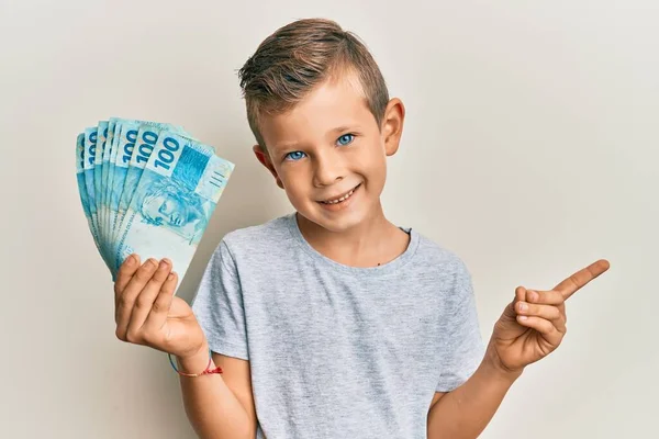 Urocze Kaukaskie Dziecko Trzymające 100 Brazylijskich Banknotów Uśmiechających Się Uśmiechem — Zdjęcie stockowe