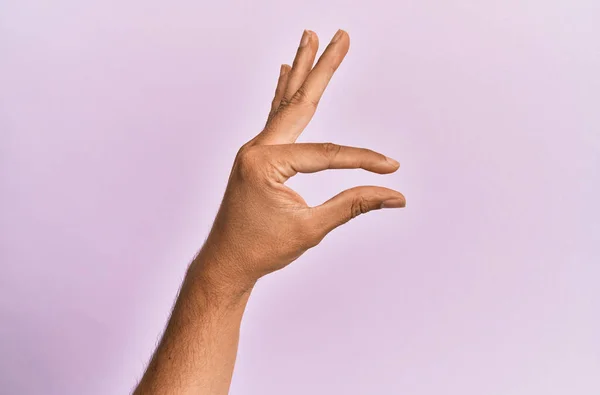 白人年轻人的胳膊和手 越过粉色孤立的背景 捡起看不见的东西 用手指握住能显示空间的物体 — 图库照片